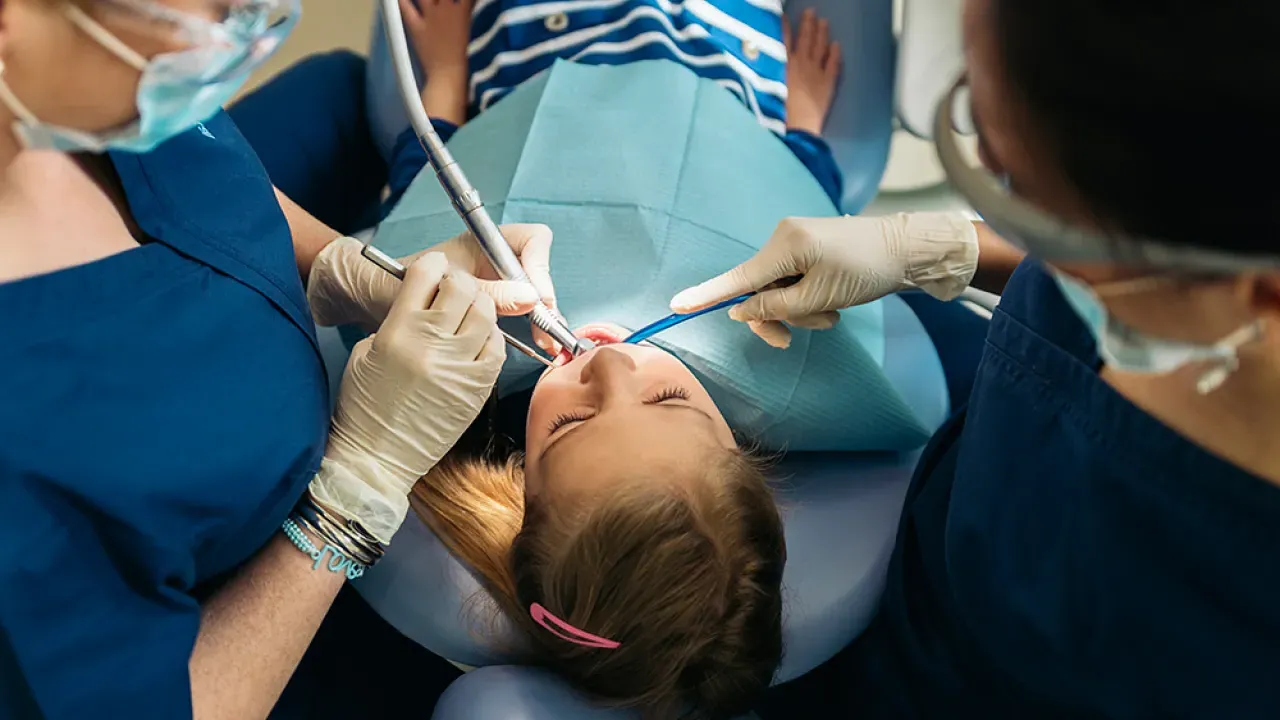 Dental assisting professionals performing a procedure on a young patient in a clinical setting, showcasing hands-on training in dental care.